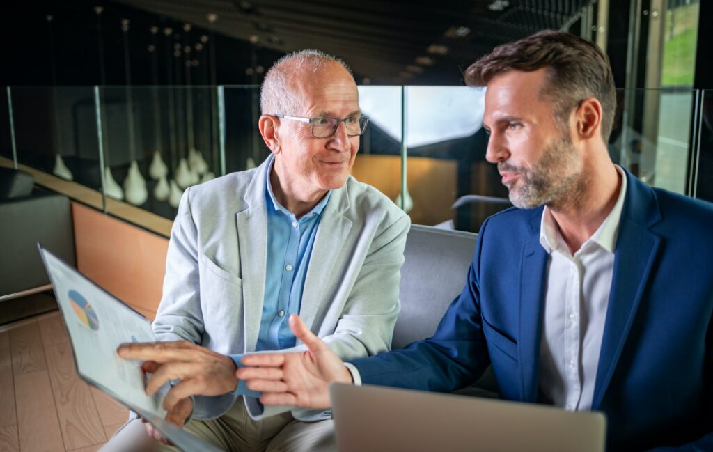 Younger and older businessman talking about documents during meeting in modern business lounge